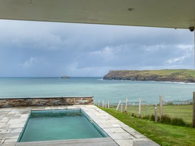 An outdoor swimming pool overlooking the sea with a grassy area and a fence by Seascape in Polzeath