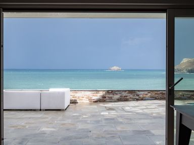 A terrace with stone flooring and white seating overlooking the sea and a rocky island at Seascape in Polzeath