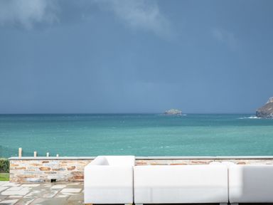 A white outdoor sofa on a stone patio facing the sea with a stone wall and an island in the distance at Seascape Polzeath