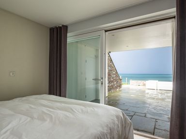 A bedroom with a bed next to sliding glass doors opening to a patio with sea view at Seascape in Polzeath