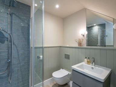 A bathroom with a shower area with blue tiles a wall-mounted toilet and a sink with a mirror at Seascape Polzeath