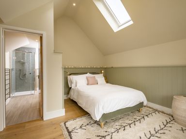 A bedroom with a bed white bedding a skylight and an ensuite bathroom with a shower at Seascape in Polzeath