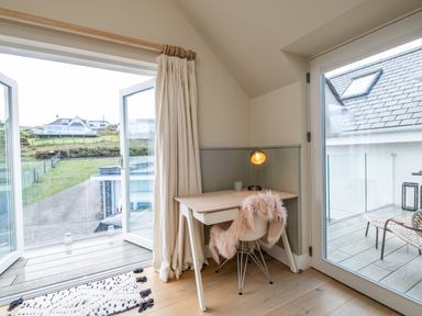 A small desk with a lamp and chair with a fur cover near glass doors opening to a balcony and outside at Seascape in Polzeath