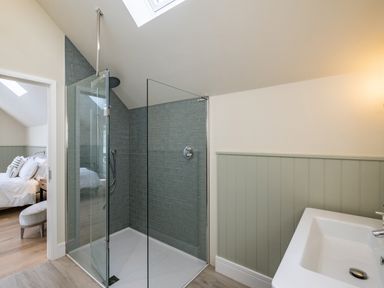 A bathroom with a glass shower enclosure a white sink and a view into a bedroom at Seascape Polzeath