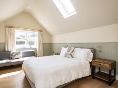 A bedroom with a double bed wooden side tables a gray sofa and a skylight at Seascape in Polzeath
