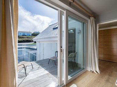 A room with wooden floor and sliding glass door leading to a balcony with chairs at Seascape Polzeath