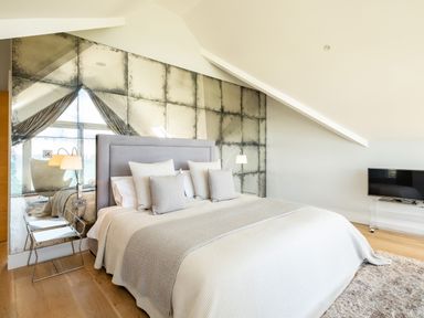 A bedroom with a large bed and multiple pillows a mirrored wall behind the bed and a television on a stand at Seascape Polzeath