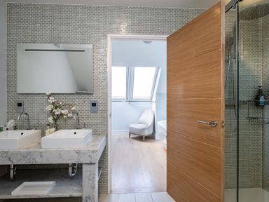A bathroom with two sinks a mirror and a glass shower with an open wooden door showing a chair and windows at Seascape Polzeath
