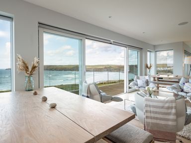A dining table with vases and stones next to a sitting area with chairs and windows showing a sea view at Seascape in Polzeath