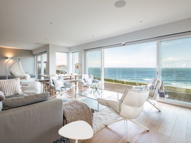 A living room with armchairs a glass coffee table and large windows overlooking the ocean at Seascape in Polzeath