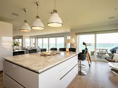 A kitchen island with marble countertop and bar stools in a room with large windows overlooking the sea at Seascape in Polzeath