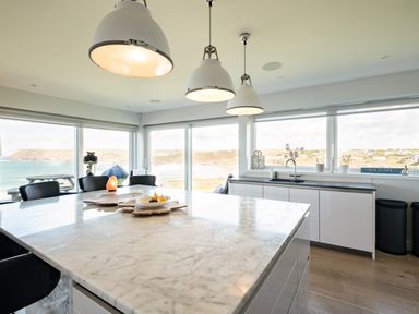 A kitchen with a large marble island and pendant lights overlooking the sea at Seascape in Polzeath