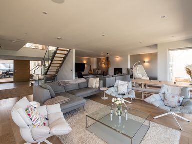A living room with gray sofas white chairs glass coffee table and a staircase at Seascape in Polzeath