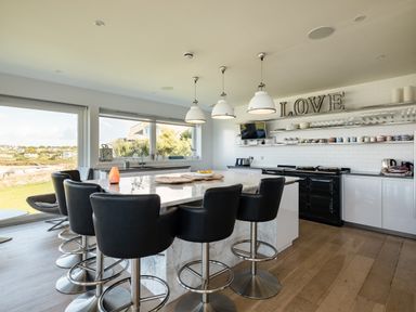 A kitchen with a marble island and black bar stools overlooking a window with a view at Seascape in Polzeath