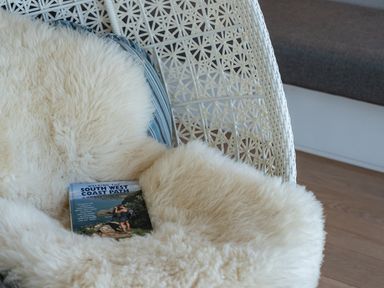 A white woven chair with a fluffy cream sheepskin and a guidebook titled Walking the South West Coast Path on it at Seascape Polzeath
