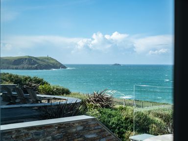 A patio with chairs overlooking the ocean and a grassy coastline at Seascape Polzeath
