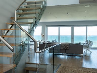 A modern living room with a staircase and large windows overlooking the sea at Seascape in Polzeath