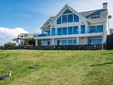 A two story house with large windows and a glass balcony on a grassy hill at Seascape in Polzeath