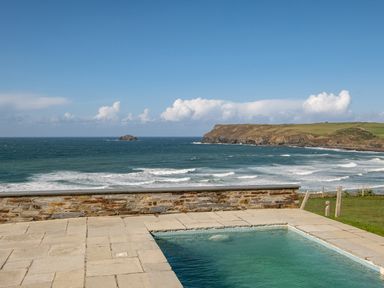 An outdoor pool with a stone patio overlooking the ocean and grassy cliffs at Seascape in Polzeath