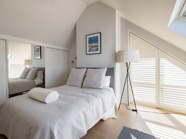 A bedroom with a bed and two pillows a rolled towel a floor lamp and window shutters at Seascape in Polzeath