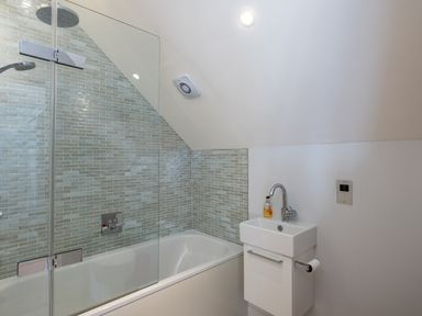 A bathroom with a bathtub a glass shower screen a small sink and a soap dispenser at Seascape in Polzeath