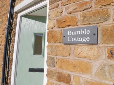 A green front door and a wall with a sign that says Bumble Cottage at Bumble Cottage in Tysoe