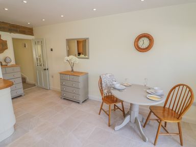 A dining area with a round table and two wooden chairs next to two gray dressers and a wall clock at Bumble Cottage in Tysoe