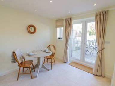 A dining area with a small round table set for two and wooden chairs near glass doors at Bumble Cottage in Tysoe