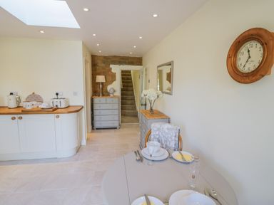 A kitchen and dining area with a round table set for two and a staircase at Bumble Cottage in Tysoe