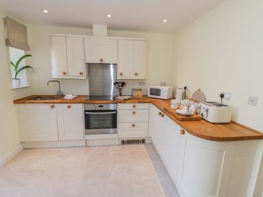 A kitchen with white cabinets wooden countertops a built in oven microwave toaster and a plant on the windowsill at Bumble Cottage in Tysoe