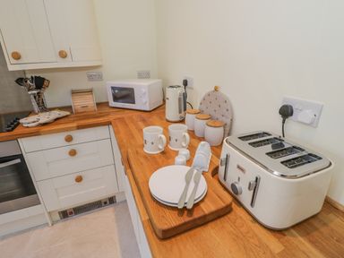 A kitchen countertop with a toaster microwave kettle mugs plates cutlery and canisters at Bumble Cottage in Tysoe