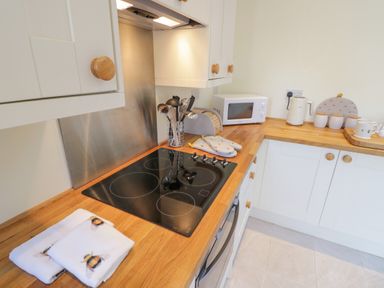 A kitchen with a black electric stovetop white cabinets wooden countertop a microwave and utensils at Bumble Cottage in Tysoe