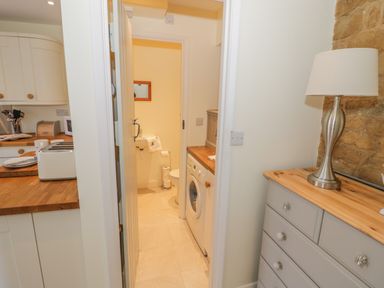 A kitchen with toaster and plates next to a utility room with washing machine and a bathroom with sink and toilet at Bumble Cottage in Tysoe