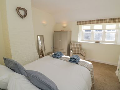 A bedroom with a bed and two blue towel sets near a wardrobe and a plaid armchair under a window at Bumble Cottage in Tysoe