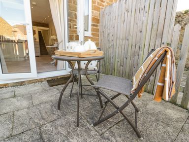 A small outdoor patio with a round table and two chairs near a wooden fence at Bumble Cottage in Tysoe