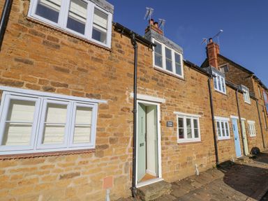 A stone cottage with white framed windows and a light green front door on a street at Bumble Cottage in Tysoe