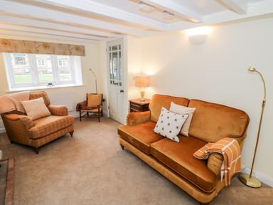 A living room with a sofa armchair small chair side table lamps and a window at Bumble Cottage in Tysoe