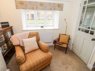 A room with an armchair and a wooden chair near a window and a wooden cabinet with glass doors at Bumble Cottage in Tysoe