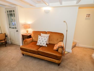 A living room with a brown sofa two cushions a side table with a lamp a floor lamp a chair and a door at Bumble Cottage in Tysoe