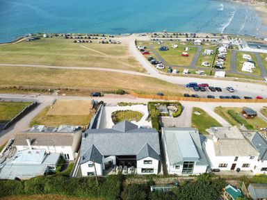 Aerial view of houses near a beach with cars parked on roads and grassy areas at Megizzy in Polzeath