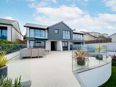 A modern two-story house with glass balcony railings and outdoor seating area at Megizzy in Polzeath