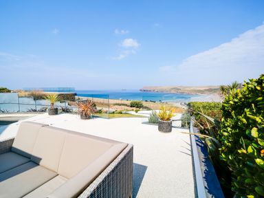 An outdoor patio with a wicker sofa and potted plants overlooking the sea and coastline at Megizzy in Polzeath