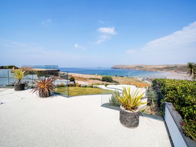 A terrace with potted plants overlooking a beach and ocean with hills in the background at Megizzy in Polzeath