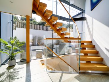 A wooden staircase with glass railings next to large windows and a potted plant at Megizzy in Polzeath