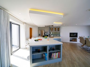 A kitchen with an island countertop and bar stools next to a dining area with chairs at Megizzy in Polzeath