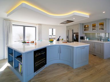 A kitchen with blue island and grey cabinets with glass doors and wood flooring at Megizzy in Polzeath