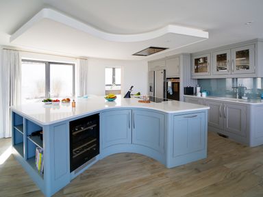A kitchen with a curved island counter with blue cabinets and white countertop at Megizzy in Polzeath