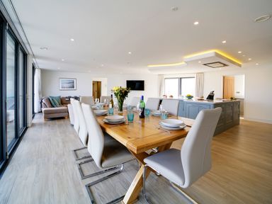 A dining table set with plates glasses and wine bottles in an open plan kitchen and living area at Megizzy in Polzeath