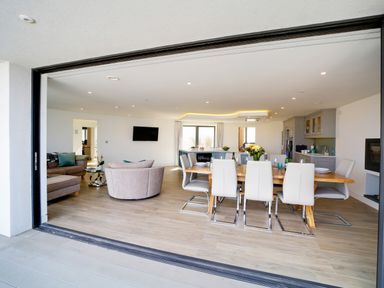 An open-concept living and dining area with a dining table and chairs a sofa set and a kitchen with cabinets Megizzy Polzeath