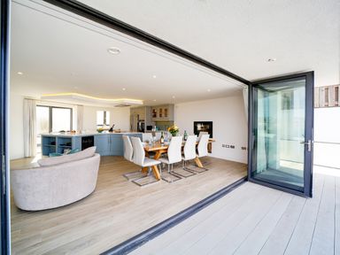 An open plan kitchen and dining area with a wooden dining table and white chairs and a circular sofa at Megizzy in Polzeath